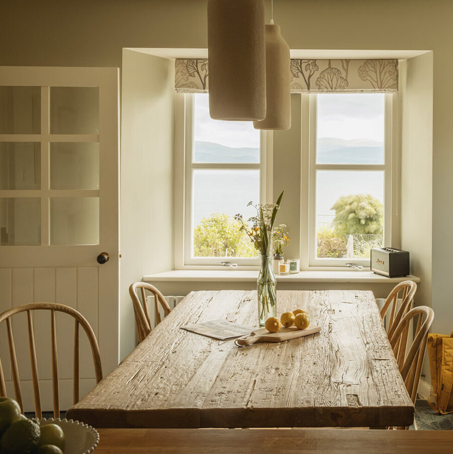 Hebridean Croft House kitchen at Mint Croft in the Isle of Skye, Scotland. Spindle-backed chairs around a traditional wooden kitchen table. Through the window a view over the sea loch - Loch Snizort.